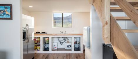 A modern kitchen with wooden beams, a built-in sink, and a window overlooking a mountainous landscape.