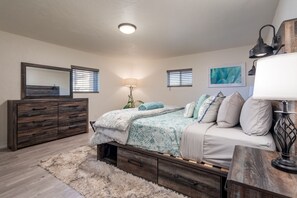 Een slaapkamer met een bed, een dressoir, een lamp en kunstwerken aan de muur.