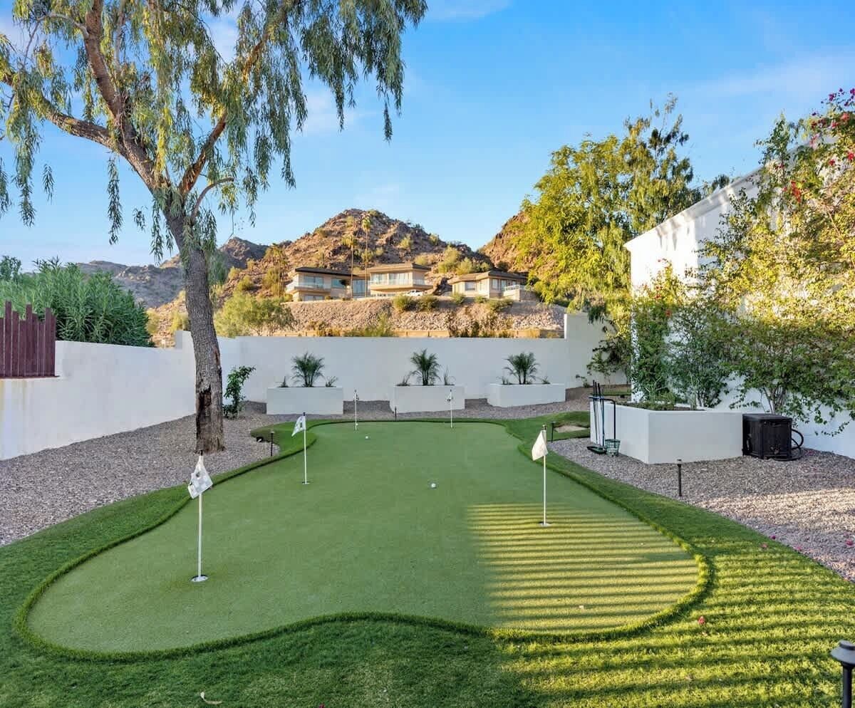 A well-maintained mini-golf course with a clear path, surrounded by landscaped areas and a white building in the background.