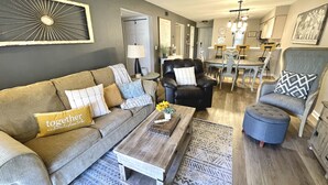 Un soggiorno con divano, poltrona, poggiapiedi, tavolino da caffè e tappeto decorato.
