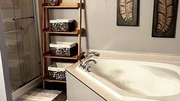A bathroom with a bathtub, a shower, a wooden shelf with baskets, and two wall-mounted feather art pieces.