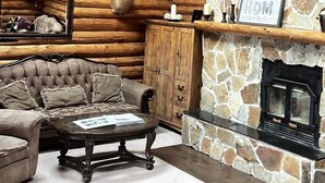 A log cabin interior with a stone fireplace, a plush sofa, a wooden cabinet, and a mounted deer head.