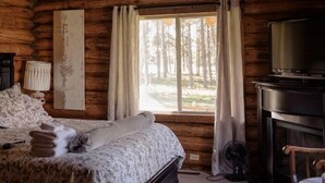 A log cabin bedroom with a bed, a television, and a fireplace.