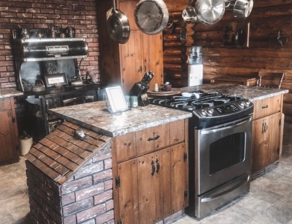 Eine rustikale Küche mit Backsteinwand, Holzschränken, einem Gasherd und einem Edelstahlbackofen.