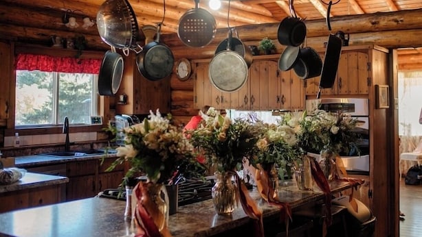 A rustic kitchen with wooden beams, hanging pots, and a central light fixture.