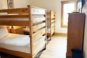 Una habitación con dos literas de madera, un armario de madera y una ventana que deja entrar luz natural.