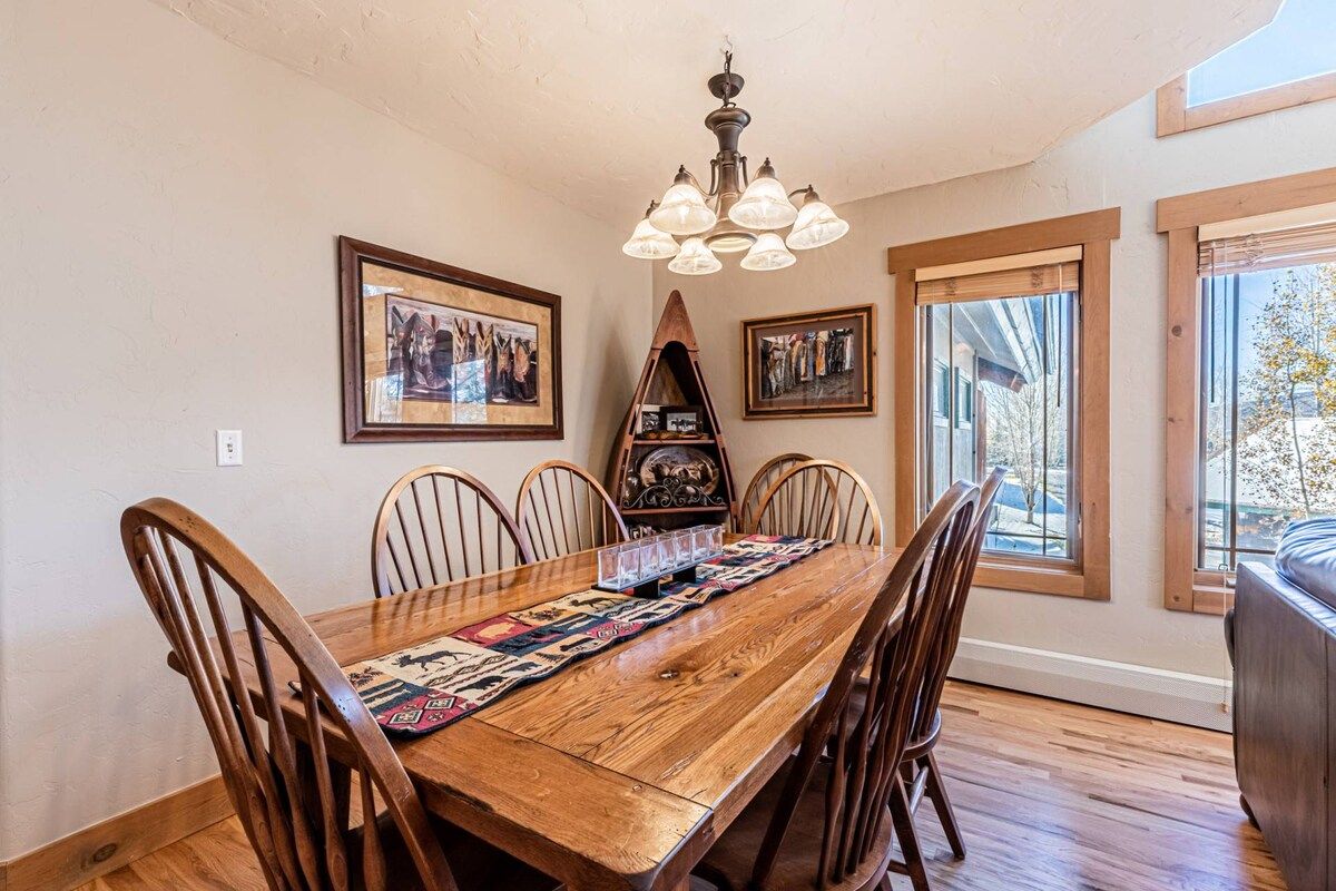 Une salle à manger avec une table en bois, six chaises, un lustre et des tableaux encadrés accrochés aux murs.