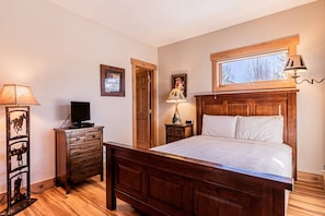 A bedroom with a wooden bed, a television on a dresser, a lamp, and a window with a view.