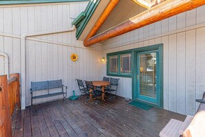 A wooden deck with a table and chairs, a bench, and a door with shutters.