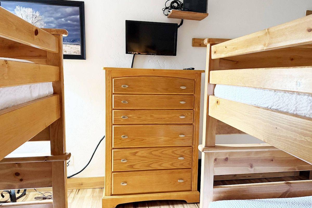 A room with a wooden dresser, a television mounted on the wall, and a bunk bed.