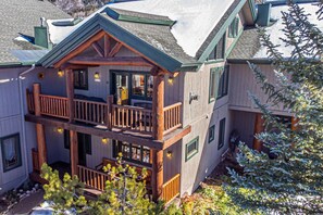A two-story wooden cabin with a balcony, a covered porch, and a snow-covered roof.