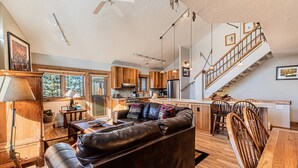 A spacious living room with a leather sofa, wooden dining table, and a kitchen area with wooden cabinets and a stainless steel refrigerator.
