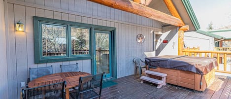 A wooden deck with a table and chairs, a hot tub, and a covered seating area.