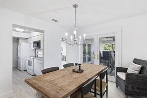 A modern kitchen with white appliances, a wooden dining table, and a wicker chair. - Santa Rosa Home with Pool, Walk to Beach & Patio (Santa Rosa Beach)
