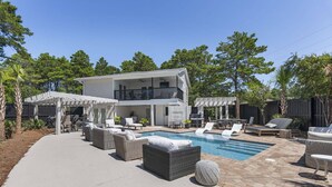 Ett modernt hus med pool, utomhusmöbler och en täckt uteplats.