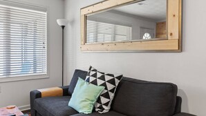A modern living room with a grey sofa, a wooden-framed mirror, and a floor lamp.