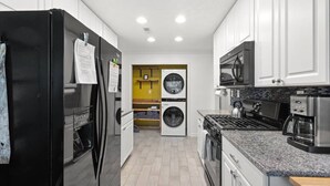 A modern kitchen with a black refrigerator, stainless steel appliances, and a yellow accent wall.