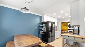 A modern kitchen with a wooden table, black refrigerator, and a yellow wall in the background.