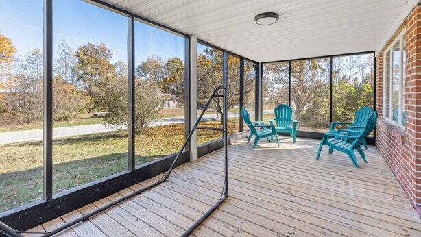 A covered outdoor area with large windows, wooden deck, and outdoor chairs.