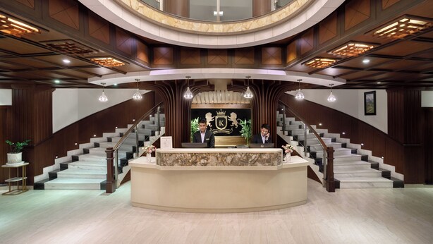 Un hall imponente con un mostrador de recepción central, una escalera curva y un techo alto con iluminación empotrada.