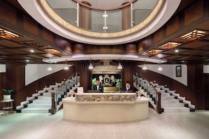 Un hall imponente con un mostrador de recepción central, una escalera curva y un techo alto con iluminación empotrada.