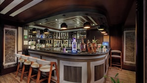 Zona de bar con mostrador curvo, taburetes de madera y luminarias colgantes.