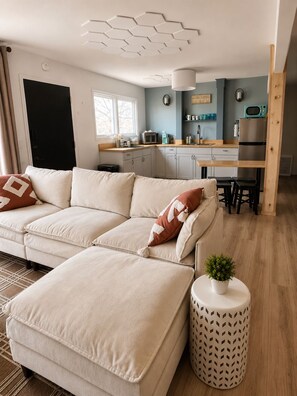 A modern living room with a sofa, a dining area, and a kitchen.