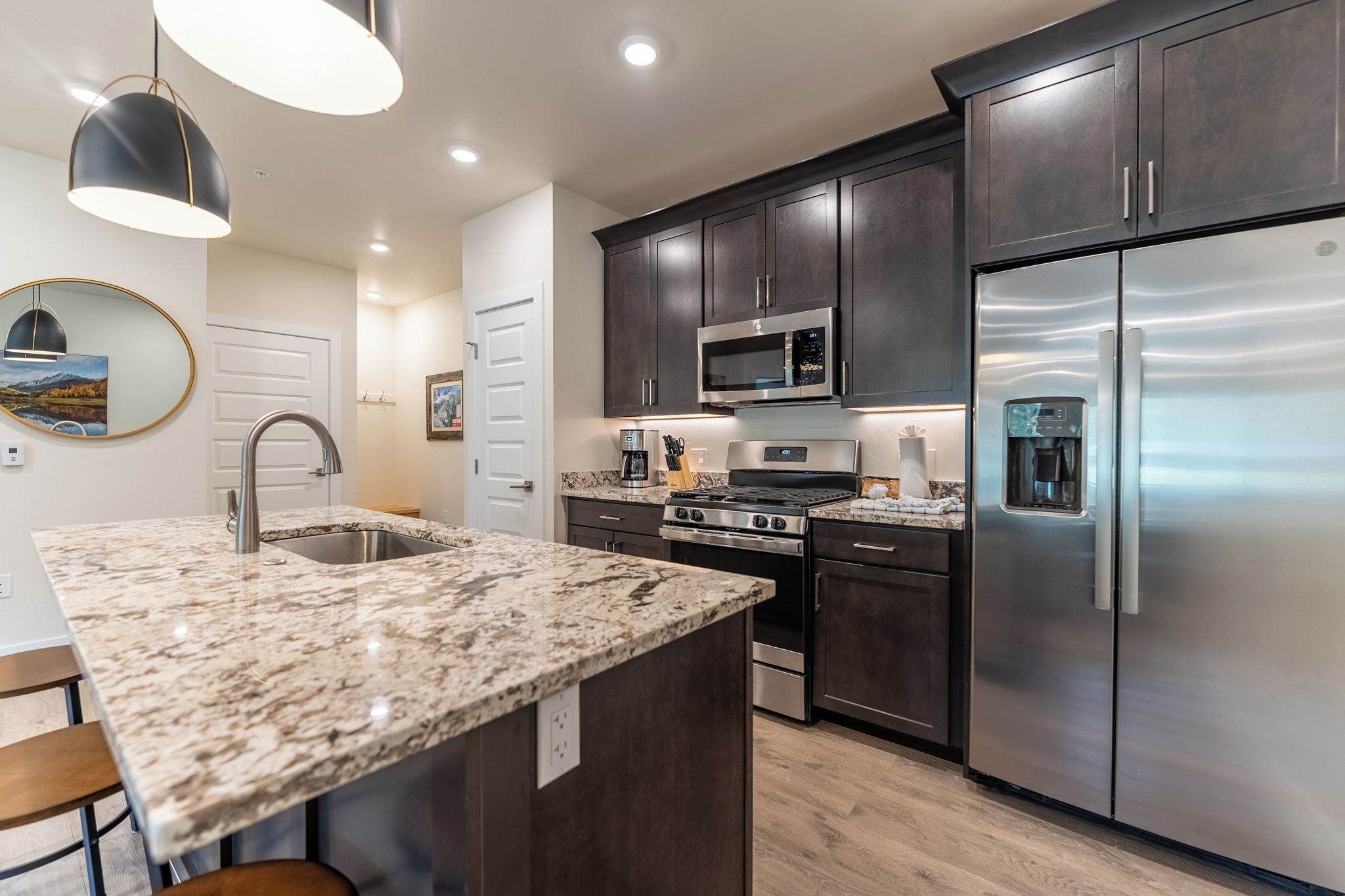 A modern kitchen with dark cabinetry, stainless steel appliances, granite countertops, and pendant lighting.