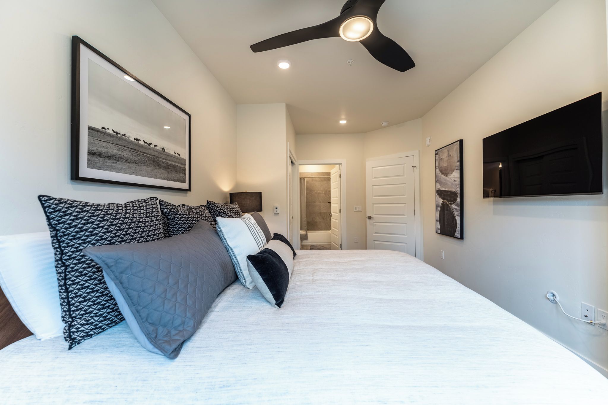 A bedroom with a bed, a ceiling fan, and a framed picture on the wall.