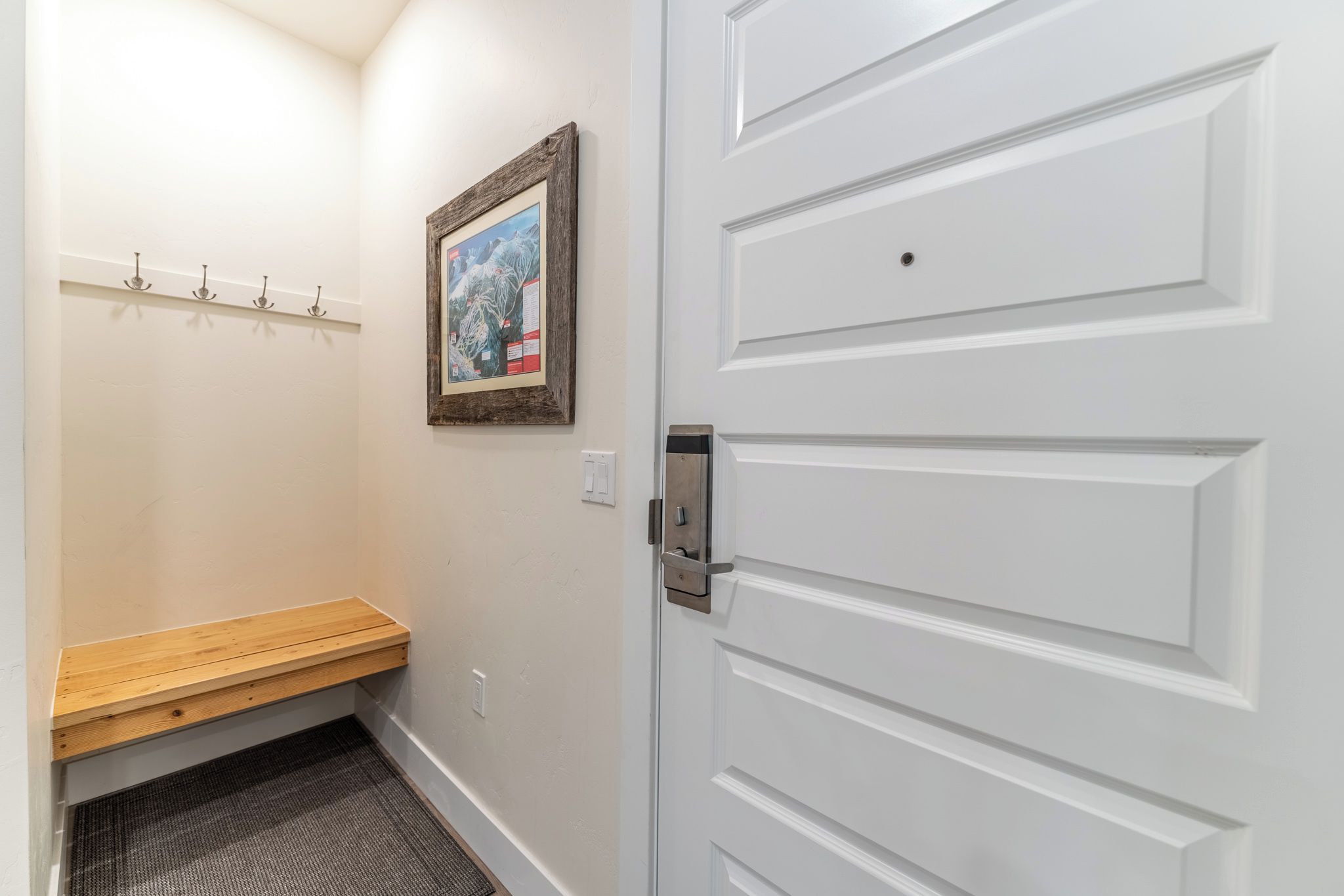 A hallway with a wooden bench, a wall-mounted picture frame, and a white door with a handle.