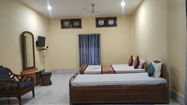 A bedroom with two single beds, a wooden chair, a small table, a mirror, a television, and a ceiling fan. - Homocation Panchami Homestay (Bokakhat)