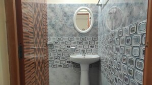 A bathroom with a patterned tile wall, a pedestal sink, a mirror, and a blue bucket on the floor. - Homocation Panchami Homestay (Bokakhat)