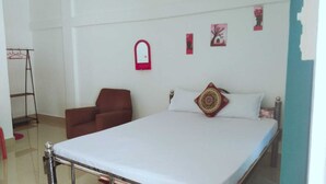 A bedroom with a bed, a red chair, a wardrobe, and a small window. - Homocation Panchami Homestay (Bokakhat)