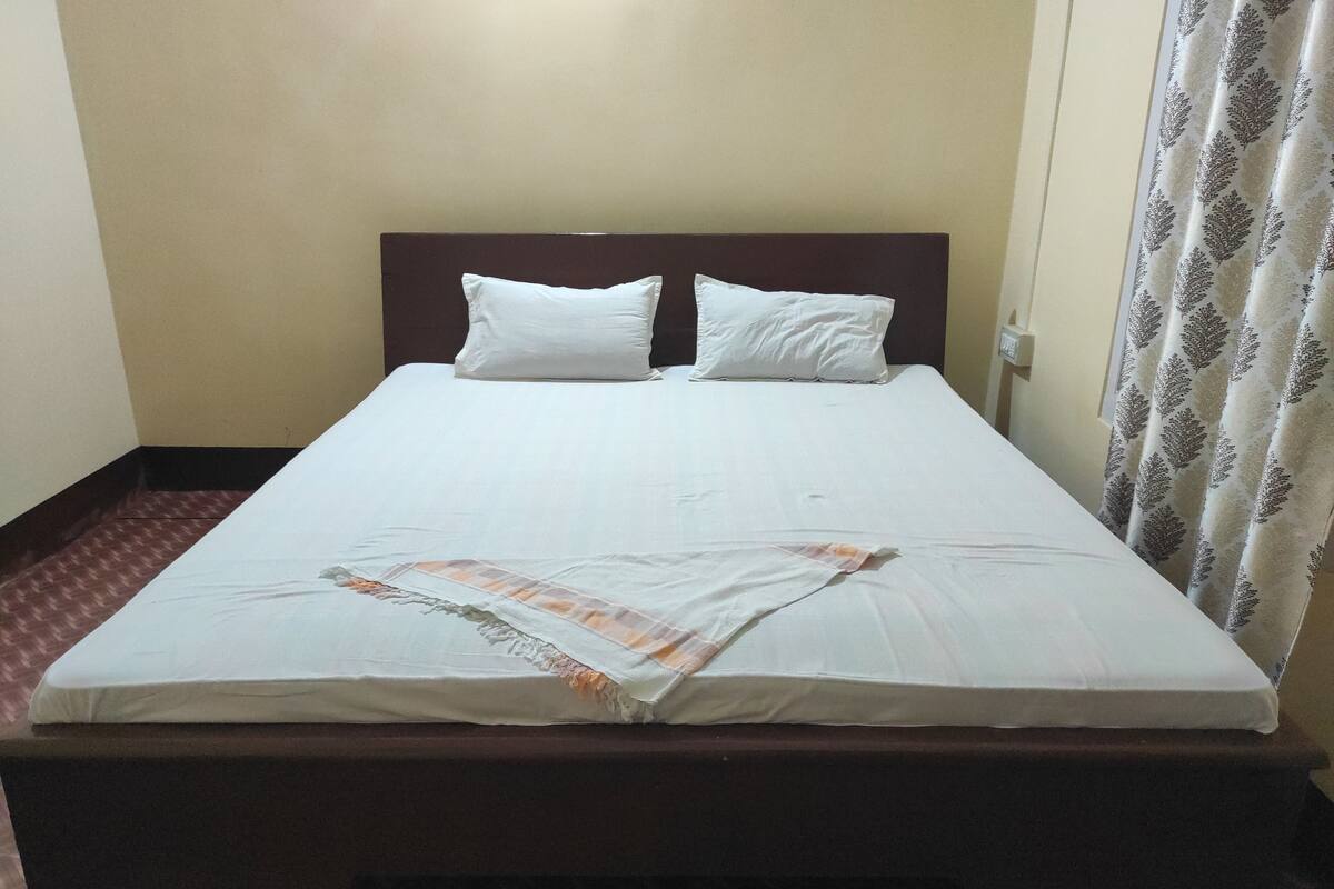 A single bed with a wooden headboard, white bedding, and a patterned curtain.
