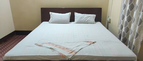 A single bed with a wooden headboard, white bedding, and a patterned curtain.