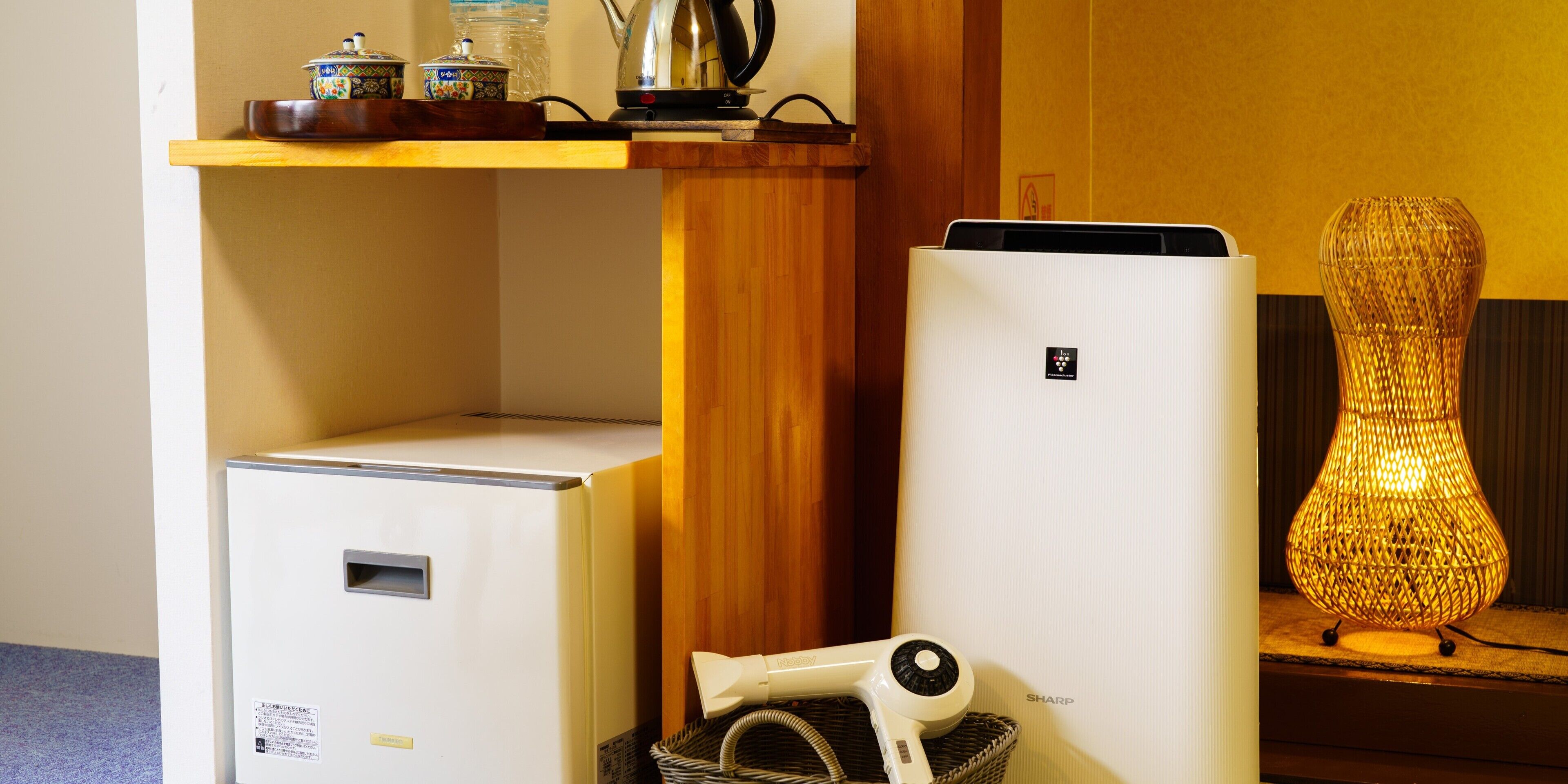 Pequeña cocina equipada con refrigerador, microondas, tetera y una cesta con secador de pelo.