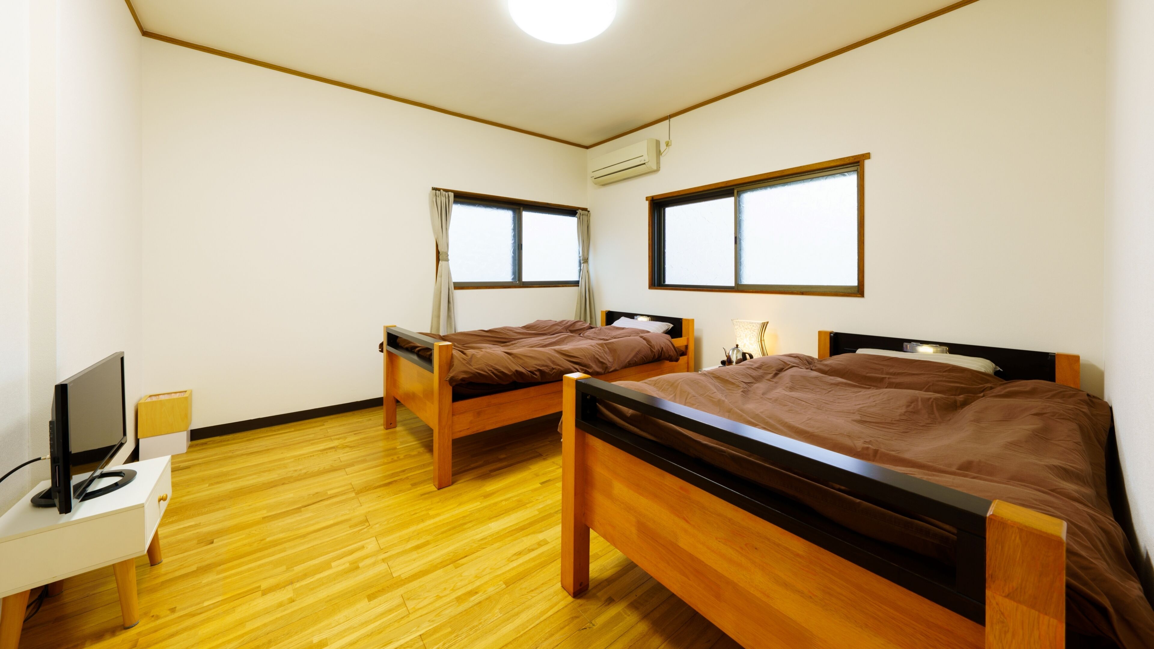 Een kamer met twee houten bedden, een bureau met een computer en een raam.