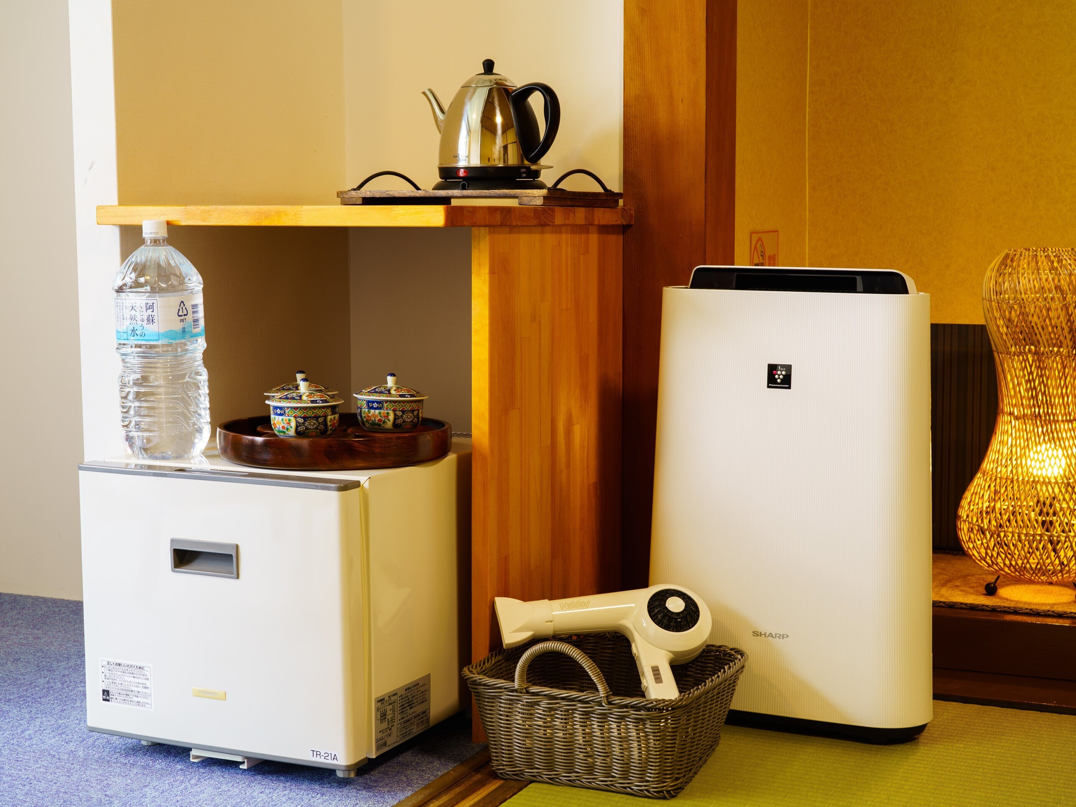 A compact kitchenette with a refrigerator, a water dispenser, a kettle, and a hairdryer.