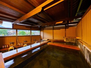 A traditional Japanese onsen with wooden beams, a wooden bench, and a view of the outside. - Kotobukiya Ryokan (Ureshino)