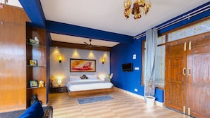 A bedroom with a bed, bedside tables, a ceiling fan, wall-mounted lights, a large window with curtains, and a wooden wardrobe. - The Junglee Bakri (Mussoorie)