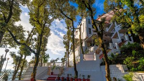 A multi-story building with a staircase leading to an upper level, surrounded by trees and potted plants. - The Junglee Bakri (Mussoorie)