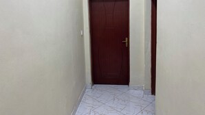 A narrow hallway with a wooden door and a white tiled floor. - Nice Rooms, Unbeatable Prices (Ruhengeri)