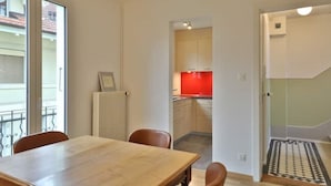 Uma área de refeições com mesa e cadeiras, um radiador e vista para uma cozinha com armários vermelhos.