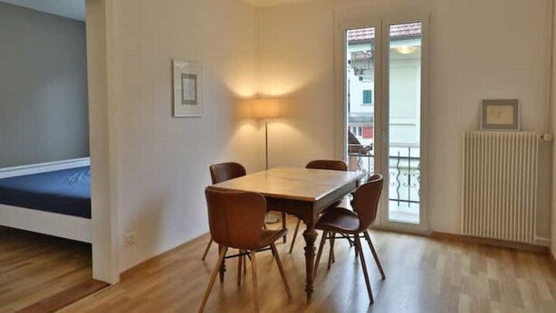 Uma área de refeições com uma mesa de madeira e quatro cadeiras, um abajur e um radiador.