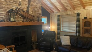 A cozy living room with a fireplace, a leather sofa, and a wooden coffee table. - 3 Cabins, 2 Acres, Private Pond, Walk to Restaurants, 4 Separate Sleeping Units (Greer)