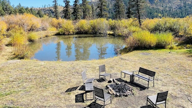 A campsite with a fire pit and benches around a pond, surrounded by trees and hills. - 3 Cabins, 2 Acres, Private Pond, Walk to Restaurants, 4 Separate Sleeping Units (Greer)