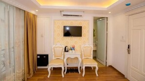 A hotel room with a wooden floor, a TV mounted on the wall, a small table with chairs, and a door leading to another room. - Cristina Boutique Hotel (Hanoi)