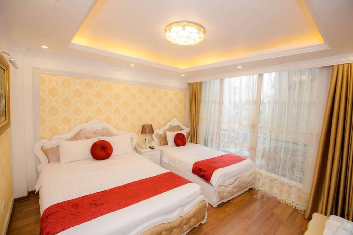 Une chambre d’hôtel avec deux lits, un lustre et une grande fenêtre avec des rideaux.