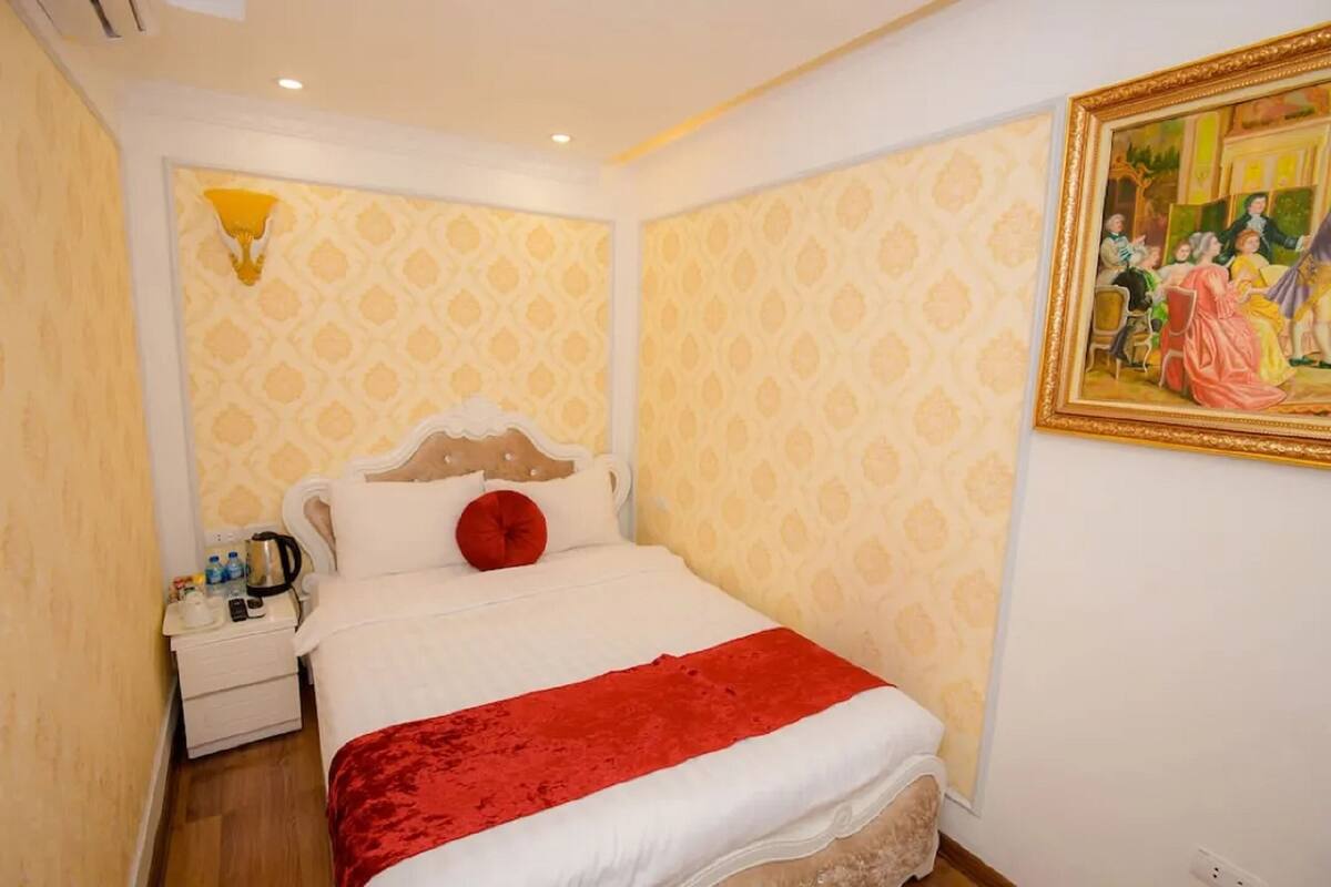 Une chambre d’hôtel avec un lit, une table de chevet, un tableau et un papier peint à motifs.