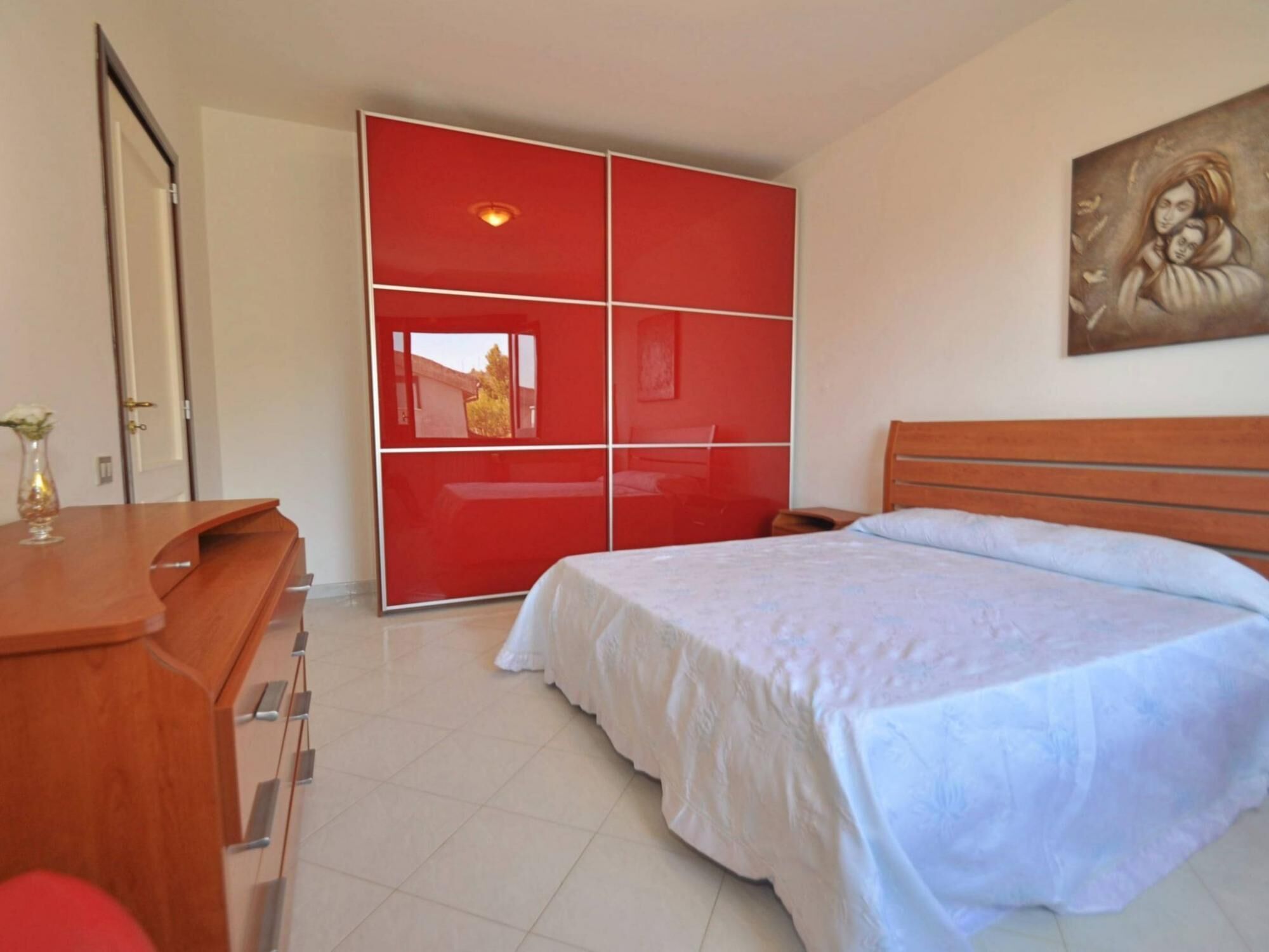 A bedroom with a bed, a desk, a chair, and a red wardrobe.